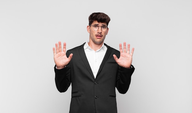 Hombre guapo joven que se siente estupefacto y asustado, por miedo a algo aterrador, con las manos abiertas al frente diciendo que se mantenga alejado