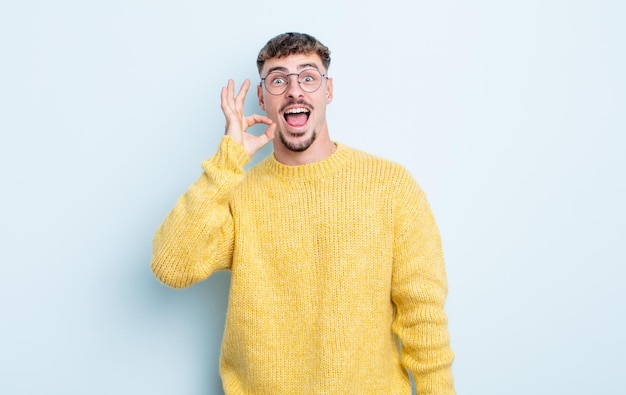 Hombre guapo joven que se siente exitoso y satisfecho, sonriendo con la boca abierta, haciendo un buen signo con la mano