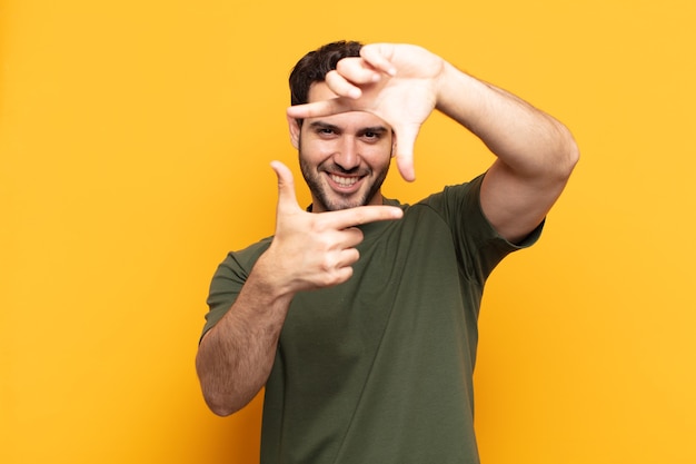 Hombre guapo joven que se siente feliz, amable y positivo, sonriendo y haciendo un retrato o un marco de fotos con las manos