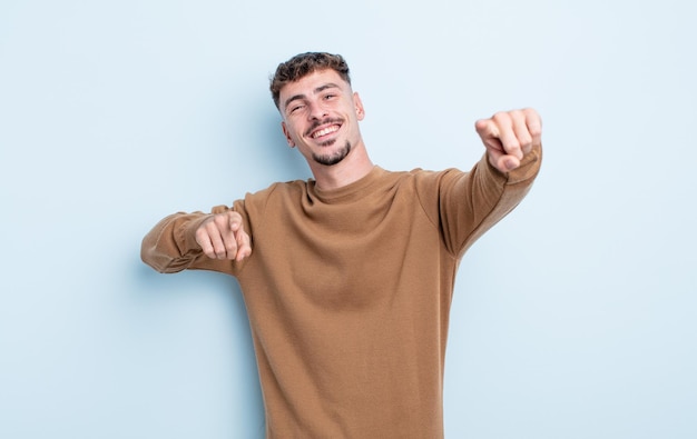 Hombre guapo joven que se siente feliz y confiado, apuntando a la cámara con ambas manos y riendo, eligiéndote