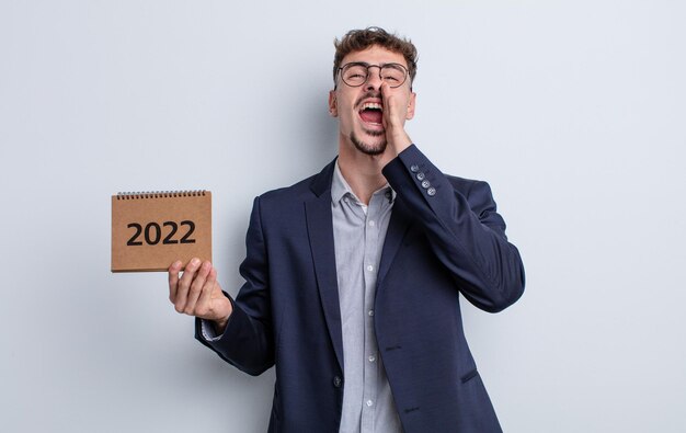 Hombre guapo joven que se siente feliz, dando un gran grito con las manos al lado de la boca. concepto de calendario