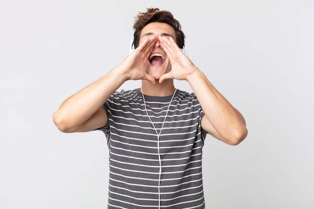 Hombre guapo joven que se siente feliz, dando un gran grito con las manos al lado de la boca. escuchar música concepto