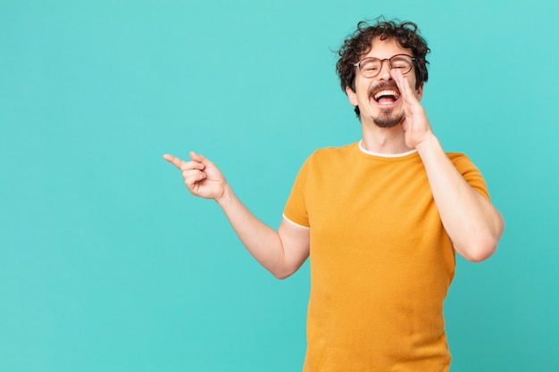 Hombre guapo joven que se siente feliz, dando un gran grito con las manos al lado de la boca