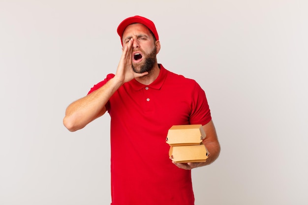 Hombre guapo joven que se siente feliz, dando un gran grito con las manos junto a la boca entregando concepto de hamburguesa