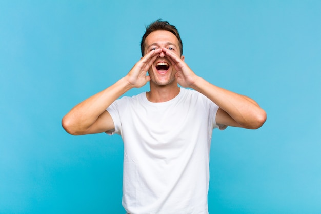 Hombre guapo joven que se siente feliz, emocionado y positivo, dando un gran grito con las manos al lado de la boca, gritando