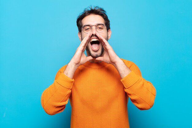 Hombre guapo joven que se siente feliz, emocionado y positivo, dando un gran grito con las manos al lado de la boca, gritando