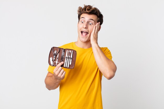 Hombre guapo joven que se siente feliz, emocionado y sorprendido y sosteniendo una caja de herramientas de uñas