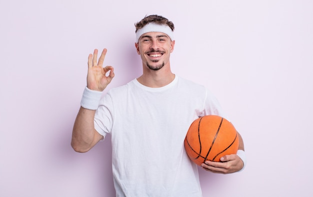 Hombre guapo joven que se siente feliz, mostrando aprobación con gesto bien. concepto de baloncesto