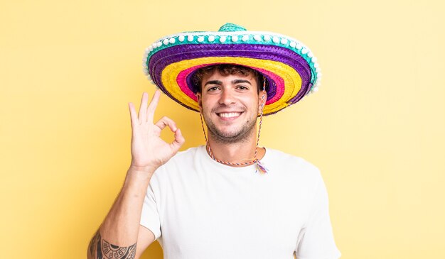 Hombre guapo joven que se siente feliz, mostrando aprobación con gesto bien. concepto de sombrero mexicano