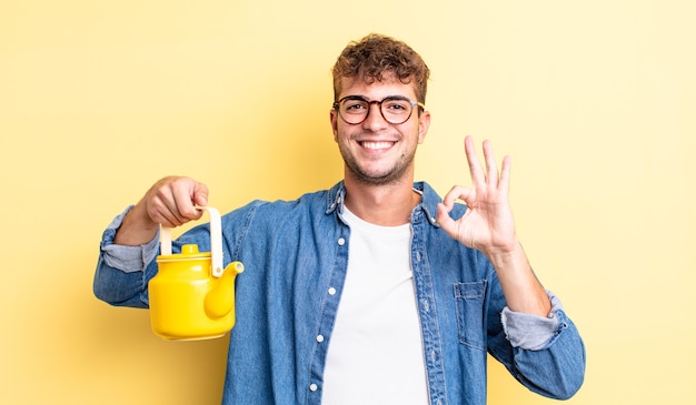 Hombre guapo joven que se siente feliz, mostrando aprobación con gesto bien concepto de tetera.