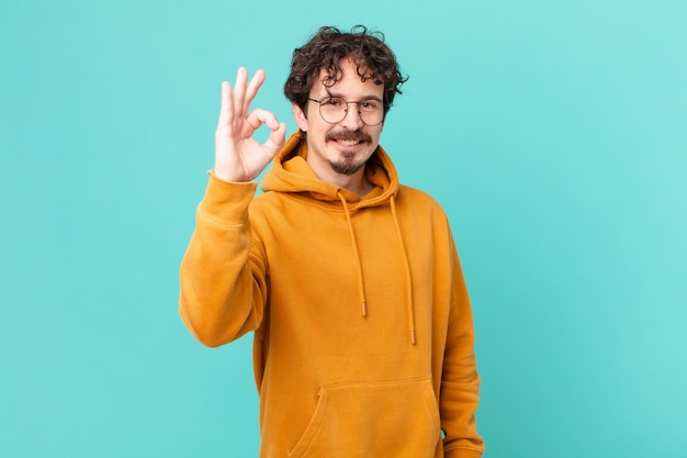 Hombre guapo joven que se siente feliz, mostrando aprobación con gesto bien