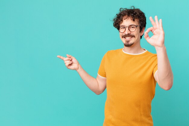 Hombre guapo joven que se siente feliz, mostrando aprobación con gesto bien