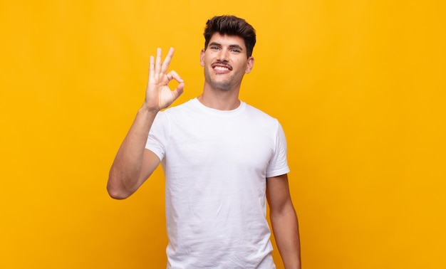 Hombre guapo joven que se siente feliz, relajado y satisfecho, mostrando aprobación con gesto bien, sonriendo