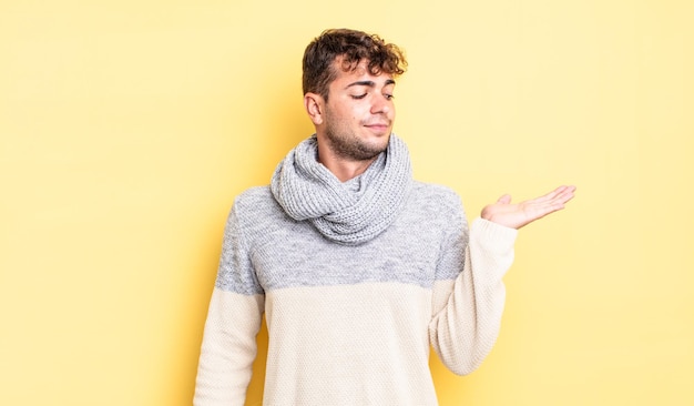 Hombre guapo joven que se siente feliz y sonriendo casualmente, mirando a un objeto o concepto sostenido en la mano al costado