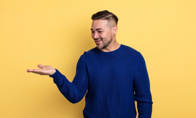 Hombre guapo joven que se siente feliz y sonriendo casualmente mirando un objeto o concepto sostenido en la mano al costado