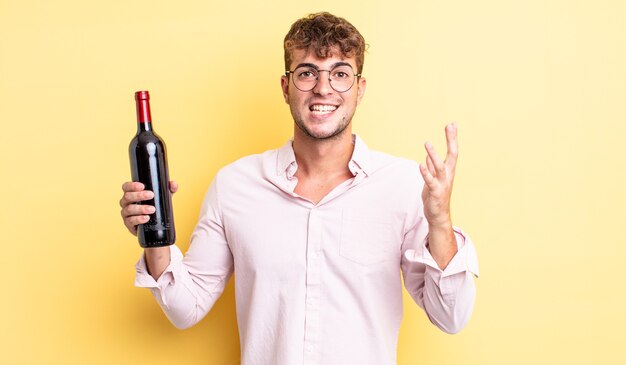 Hombre guapo joven que se siente feliz, sorprendido al darse cuenta de una solución o idea. concepto de botella de vino