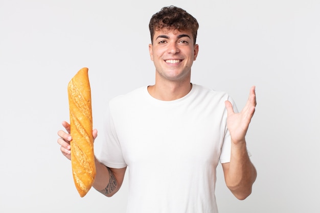 Hombre guapo joven que se siente feliz, sorprendido al darse cuenta de una solución o idea y sosteniendo una barra de pan