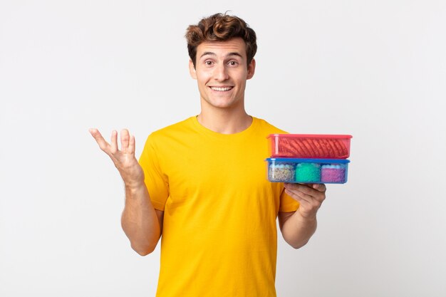 Hombre guapo joven que se siente feliz, sorprendido al darse cuenta de una solución o idea y sosteniendo loncheras