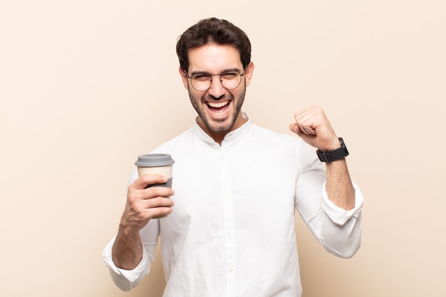 Hombre guapo joven que se siente feliz, sorprendido y orgulloso, gritando y celebrando el éxito con una gran sonrisa