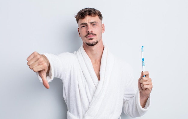 Hombre guapo joven que se siente mostrando los pulgares hacia abajo el concepto de cepillo de dientes