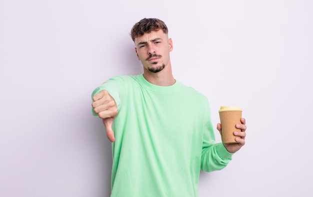 Hombre guapo joven que se siente mostrando los pulgares hacia abajo para llevar el concepto de café