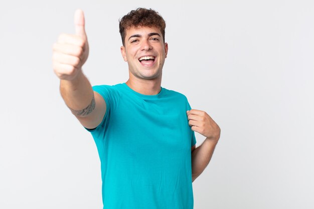 Foto hombre guapo joven que se siente orgulloso, despreocupado, seguro y feliz, sonriendo positivamente con los pulgares hacia arriba