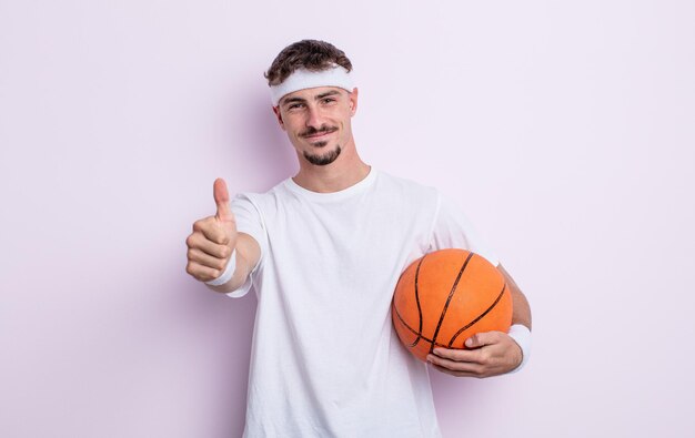 Hombre guapo joven que se siente orgulloso, sonriendo positivamente con los pulgares hacia arriba. concepto de baloncesto