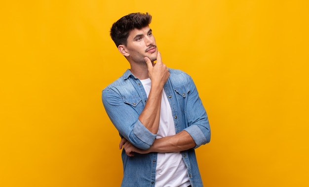 Hombre guapo joven que se siente pensativo, preguntándose o imaginando ideas, soñando despierto y mirando hacia arriba para copiar el espacio