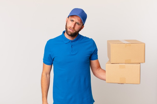 Hombre guapo joven que se siente perplejo y confundido. concepto de entrega de paquetes