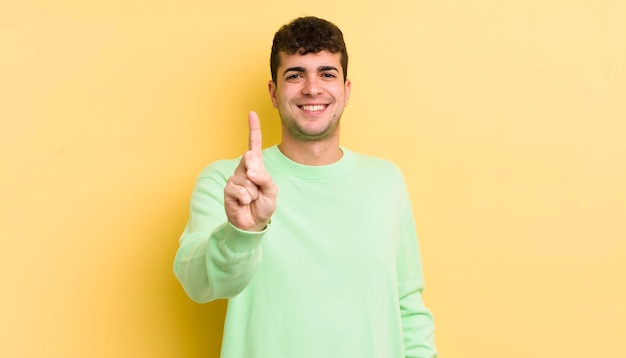 Hombre guapo joven que sonríe con orgullo y confianza haciendo la pose número uno triunfalmente sintiéndose como un líder