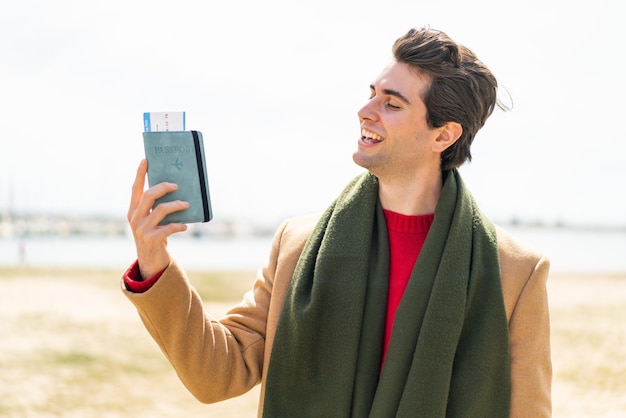 Hombre guapo joven que sostiene un pasaporte al aire libre con expresión feliz