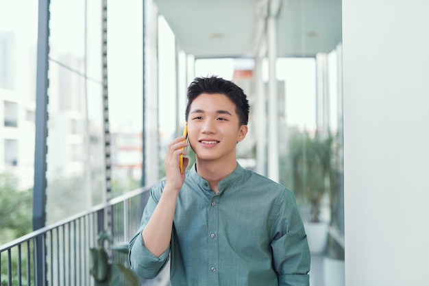 Hombre guapo joven que tiene una conversación en el teléfono inteligente en el balcón en un día soleado de verano