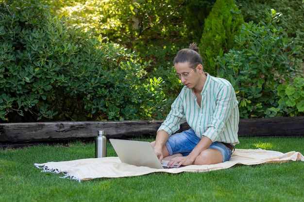 Hombre guapo joven que trabaja como nómada digital en el parque de la ciudad y la naturaleza en cualquier parte del mundo