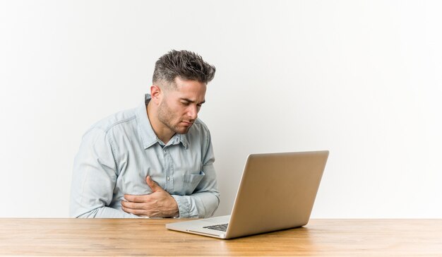 Hombre guapo joven que trabaja con su computadora portátil enfermo, que sufre de dolor de estómago, concepto de enfermedad dolorosa.