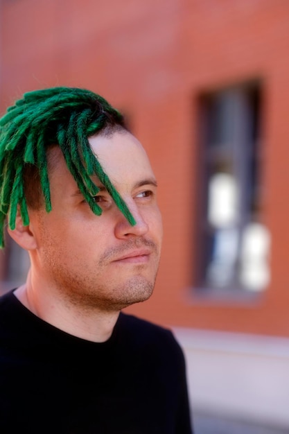 Hombre guapo joven con rastas verdes en camiseta negra posando en la calle de la ciudad