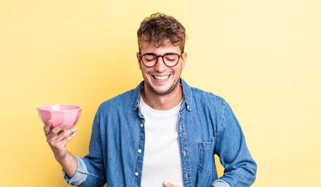 Hombre guapo joven riendo a carcajadas de una broma hilarante. concepto de cuenco vacío