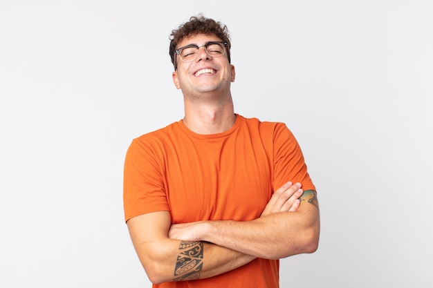 Hombre guapo joven riendo felizmente con los brazos cruzados, con una pose relajada, positiva y satisfecha