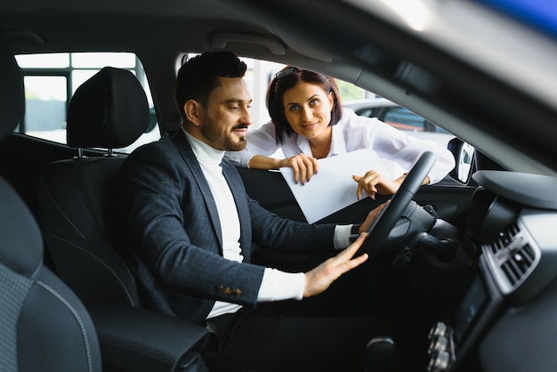 Hombre guapo joven en la sala de exposiciones de pie cerca del coche