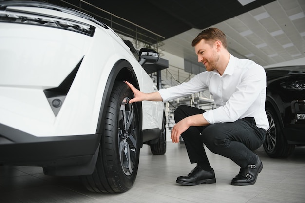 Hombre guapo joven en la sala de exposiciones de pie cerca del coche