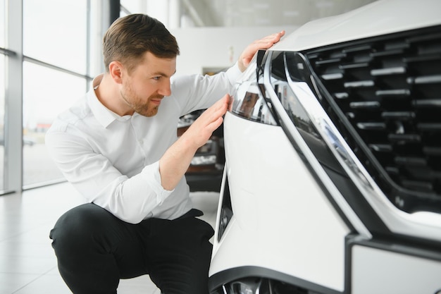 Hombre guapo joven en la sala de exposiciones de pie cerca del coche