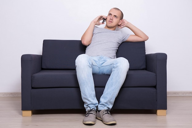 Foto hombre guapo joven sentado en el sofá y hablando por teléfono móvil