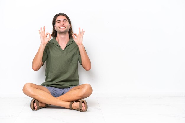 Foto hombre guapo joven sentado en el suelo aislado sobre fondo blanco en pose zen