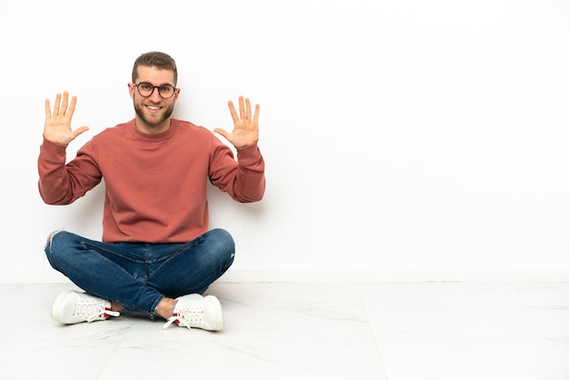 Foto hombre guapo joven sentado en el suelo contando diez con los dedos
