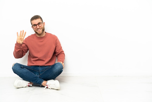 Hombre guapo joven sentado en el suelo feliz y contando cuatro con los dedos