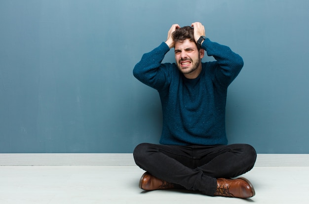 Hombre guapo joven sentado en el suelo, sintiéndose frustrado y molesto, enfermo y cansado de fracasar, harto de tareas aburridas y aburridas