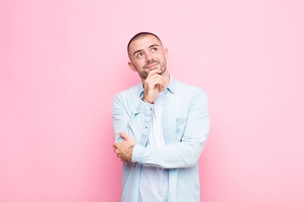 Hombre guapo joven sintiéndose pensativo, preguntándose o imaginando ideas, soñando despierto y mirando hacia arriba para copiar el espacio sobre la pared