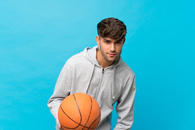 Hombre guapo joven sobre azul aislado con pelota de baloncesto