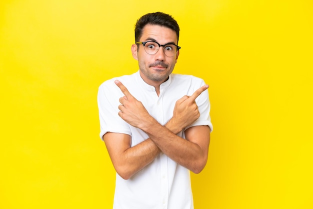 Hombre guapo joven sobre fondo amarillo aislado apuntando a los laterales que tienen dudas