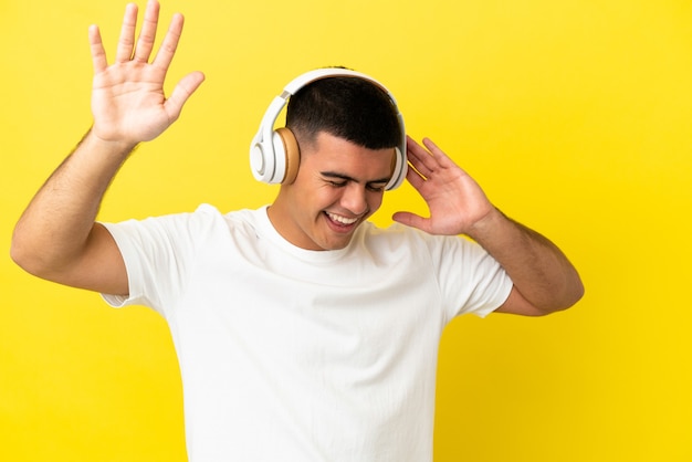 Hombre guapo joven sobre fondo amarillo aislado escuchando música y bailando