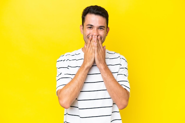 Hombre guapo joven sobre fondo amarillo aislado feliz y sonriente cubriendo la boca con las manos